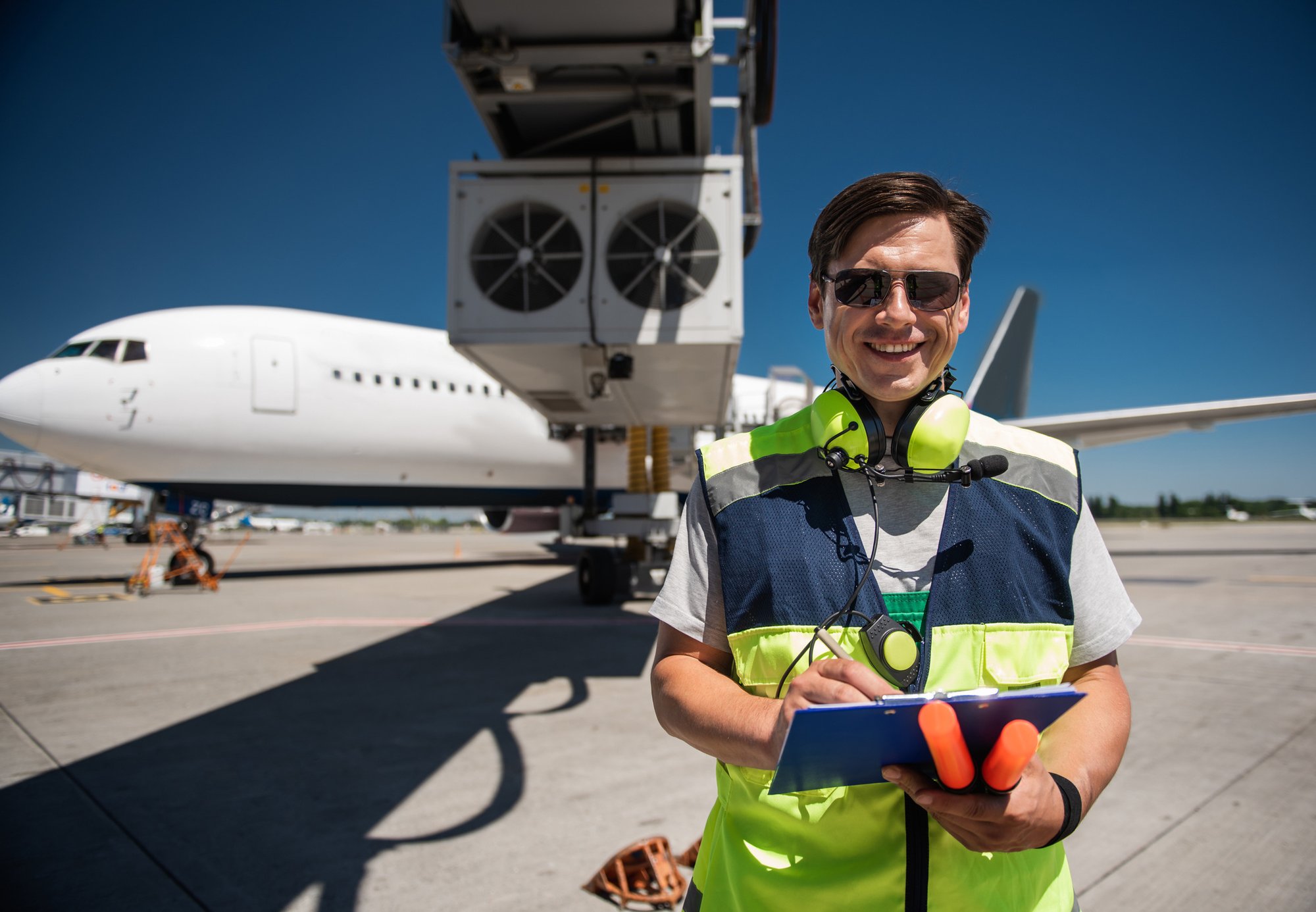 Airport-worker-looking-at-camera-with-smile-while-writing-on-clipboard-1141642779_2083x1444
