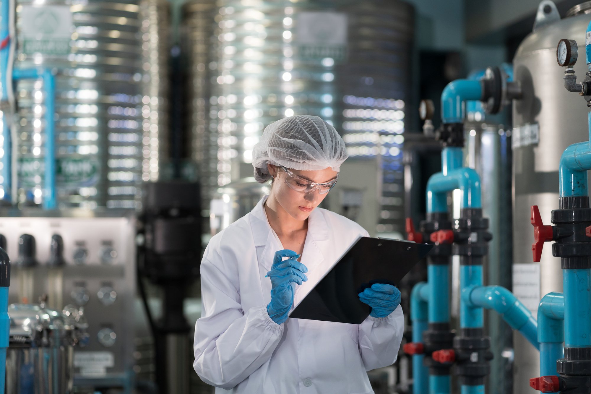 Female-worker-wearing-uniform,-hairnet-working-and-checking-of-water-pump-system,-pipes-station,-Water-pressure-system,-water-tank-at-production-line-in-industry-factory-1784055413_2125x1416