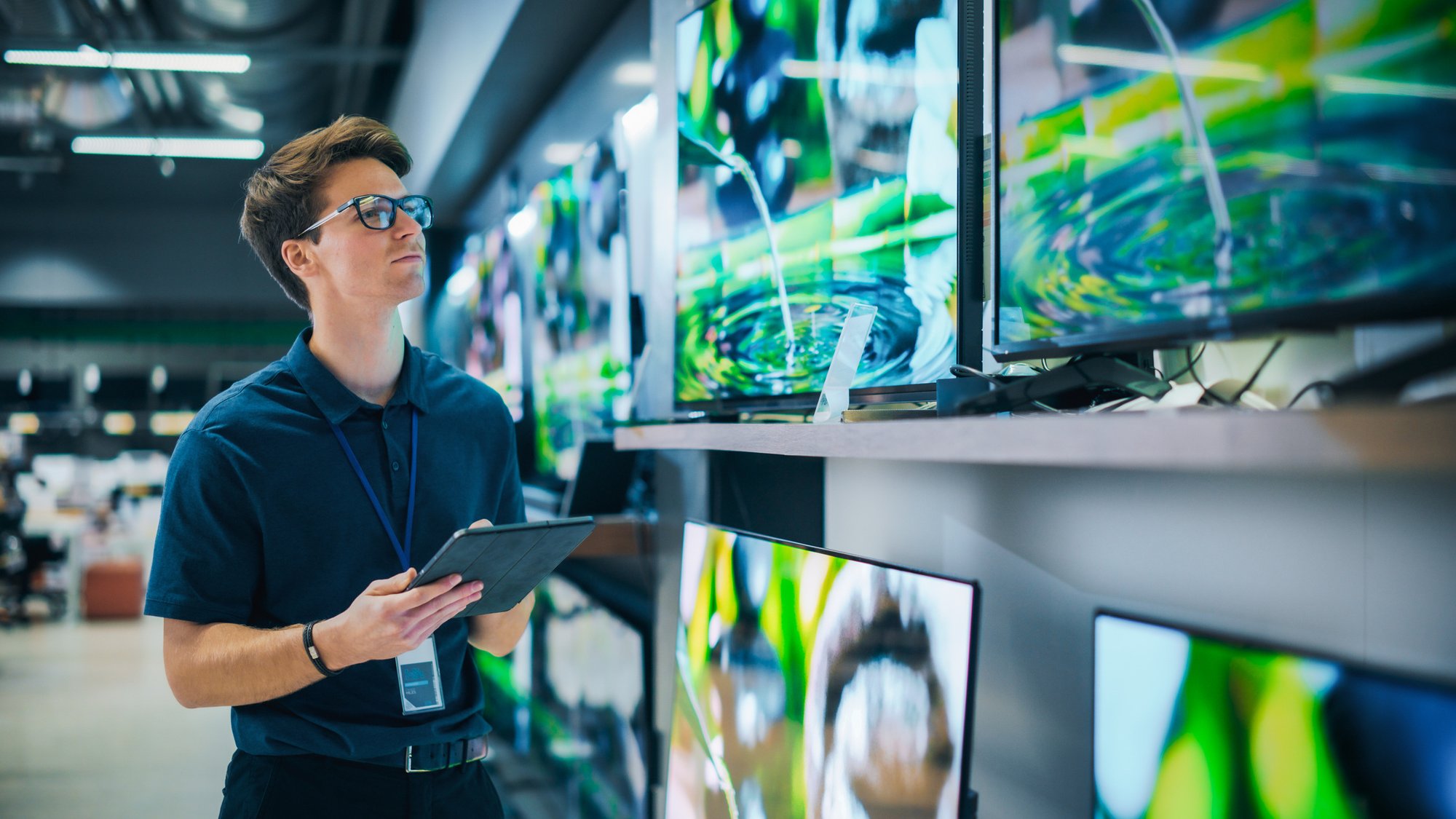 Young-Sales-Manager-in-Home-Electronics-Store-Expertly-Manages-Operations-Using-Tablet-Computer.-Professional-Oversees-TV-Sets-Inventory-and-Product-Updates-with-Technological-Efficiency-2065410352_2313x1301