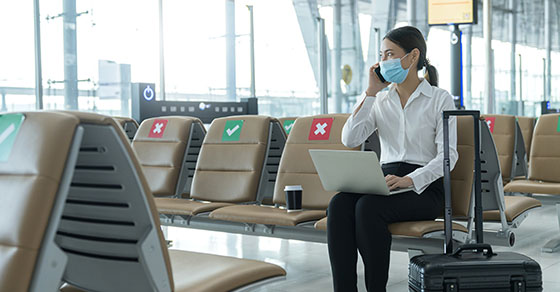 woman sitting in airport wearing mask with laptop