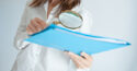 woman holding magnifying glass over blue folder
