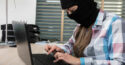 woman wearing black ski mask typing on laptop