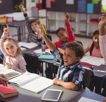 schoolkids raising their hands in classroom