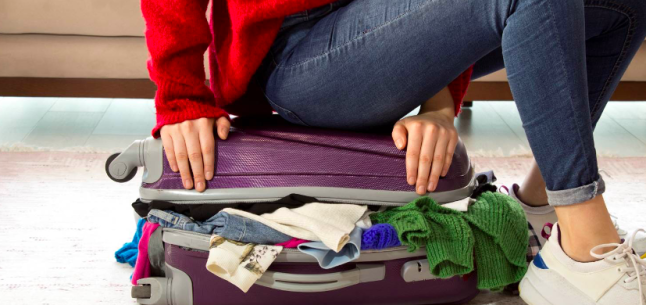 woman sitting on full suitcase